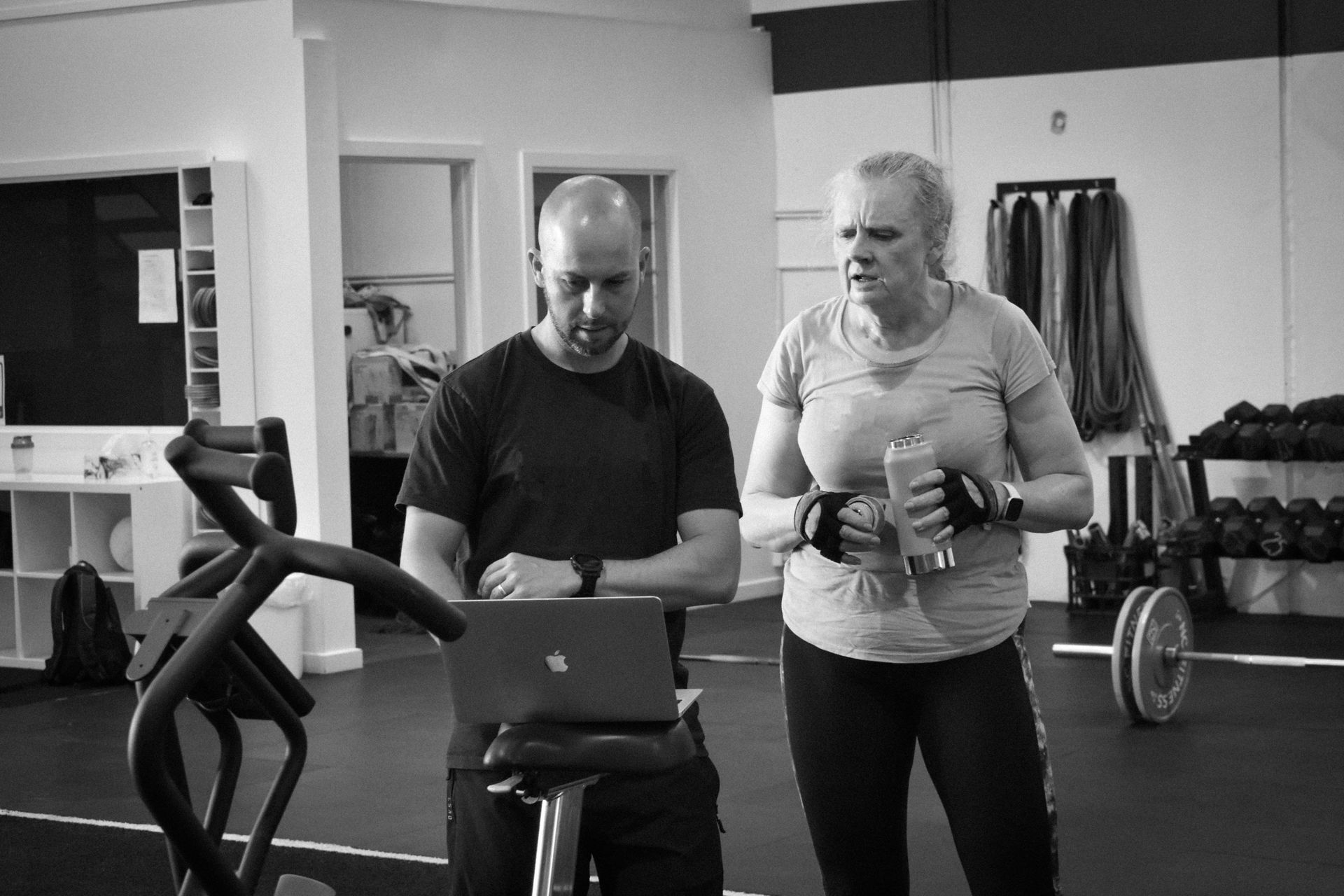 A man and a woman are looking at a laptop in a gym.