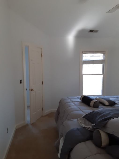 Bedroom with bed, open door to a room, window with blinds, and white walls.