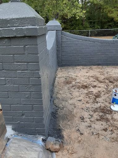 Gray painted brick wall with pillars, partly painted with a sandy ground in front.