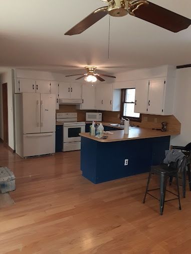 Kitchen with white cabinets, navy island, wood floor, and ceiling fan.