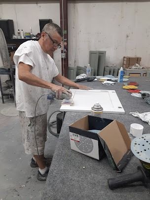 Man sanding a white cabinet door in a workshop, with a box of sanding discs nearby.