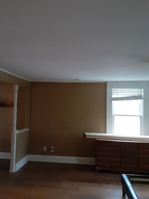 Empty room with tan walls, white trim, wood dresser, and window with blinds.