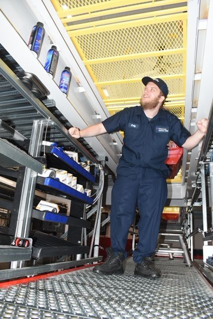 A man in a blue uniform is standing in an oil change service area smiling