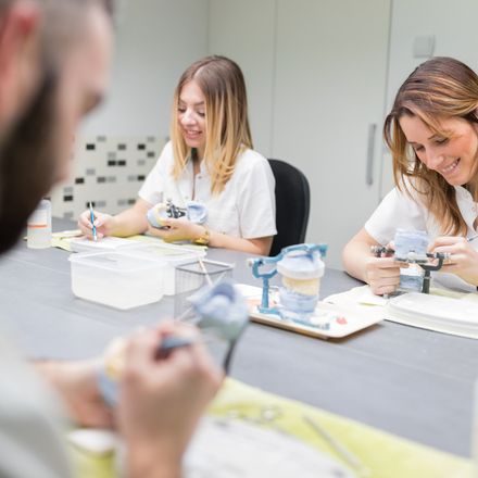 A man and two women are sitting at a table working on dental models