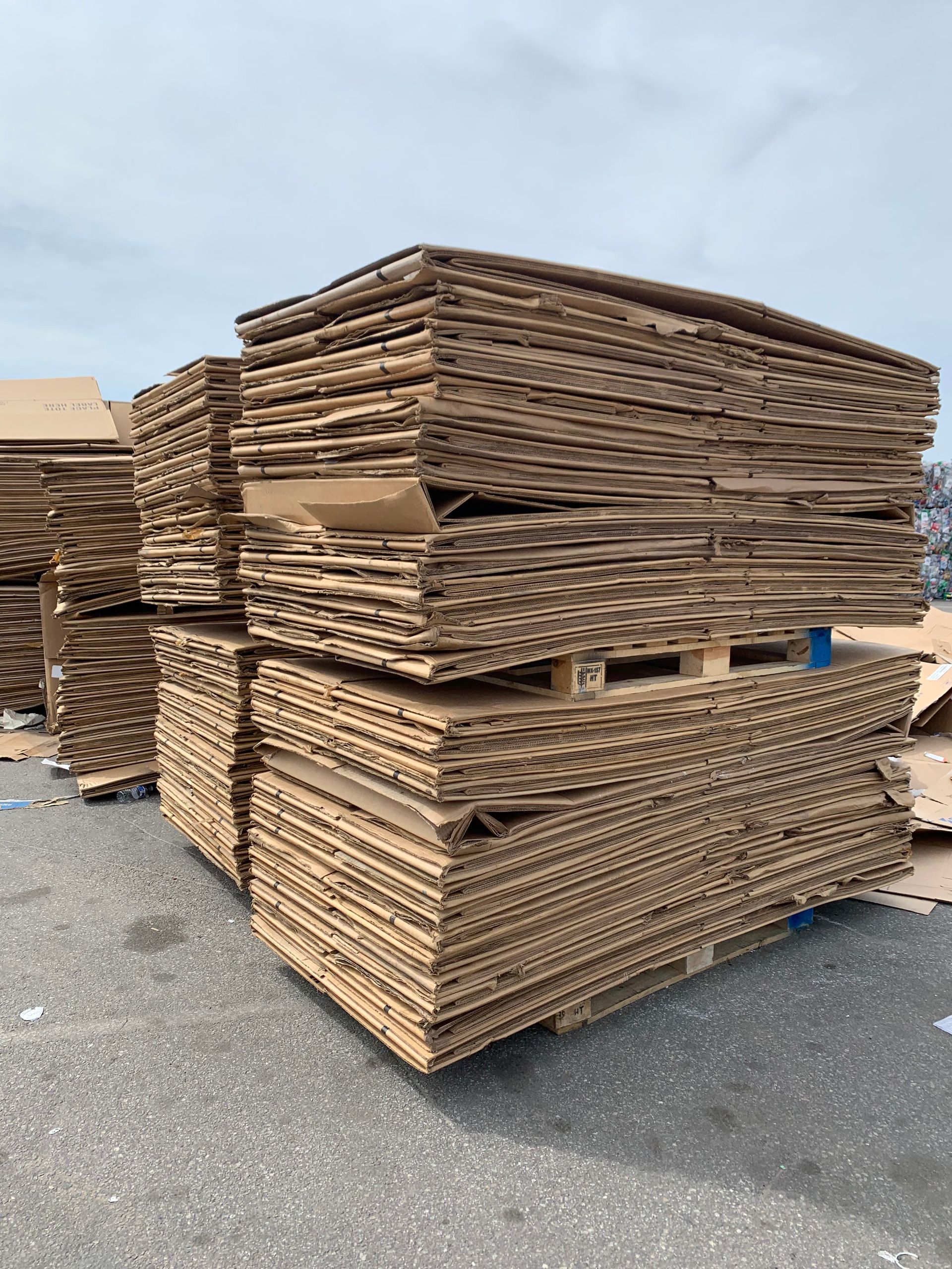 Stacks of flattened cardboard boxes on pallets, outdoors.