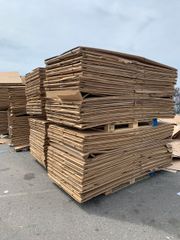 Stacks of flattened cardboard boxes on pallets, outdoors.