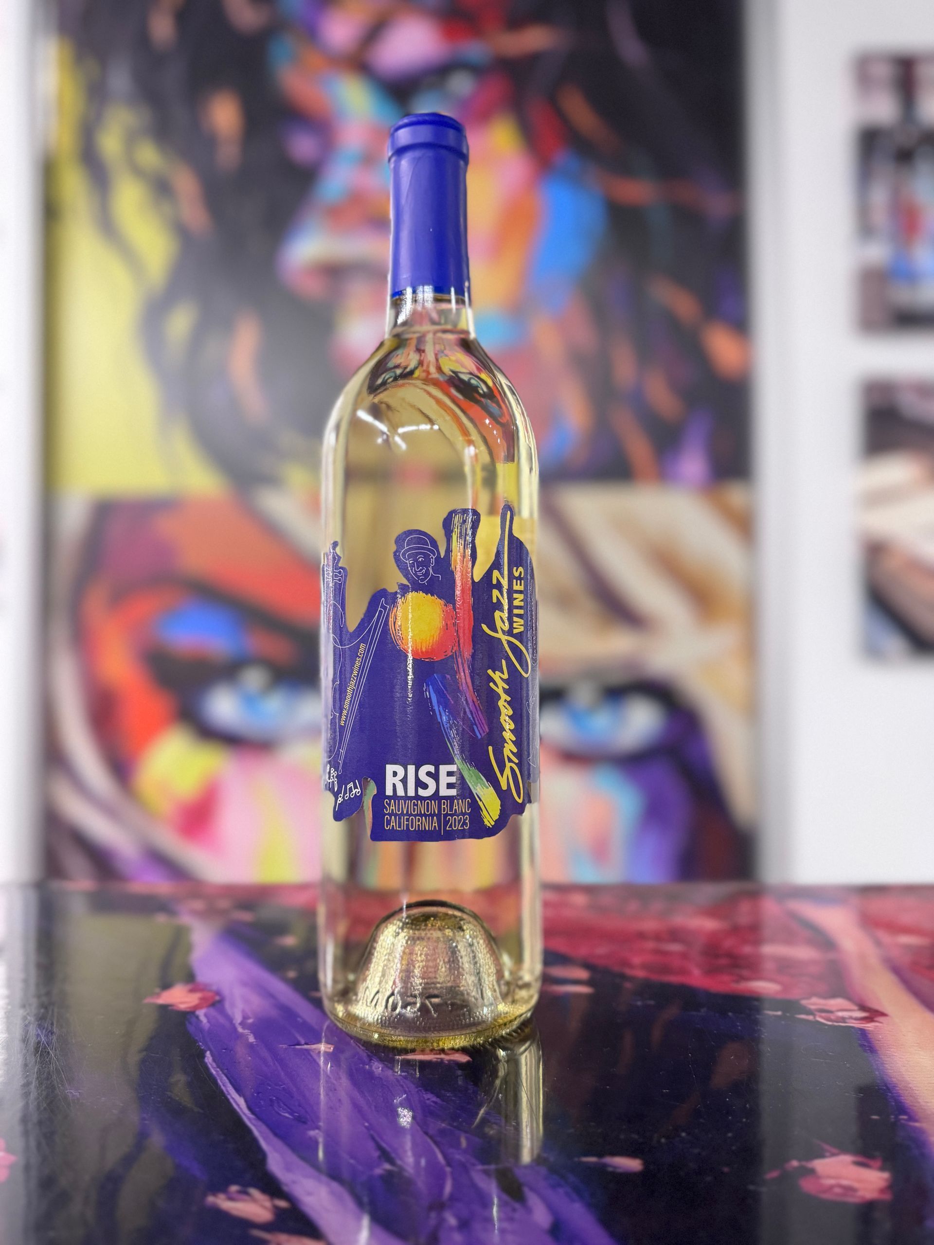 A bottle of white wine with a blue label featuring a yellow sun graphic, standing on a colorful, abstract art surface.