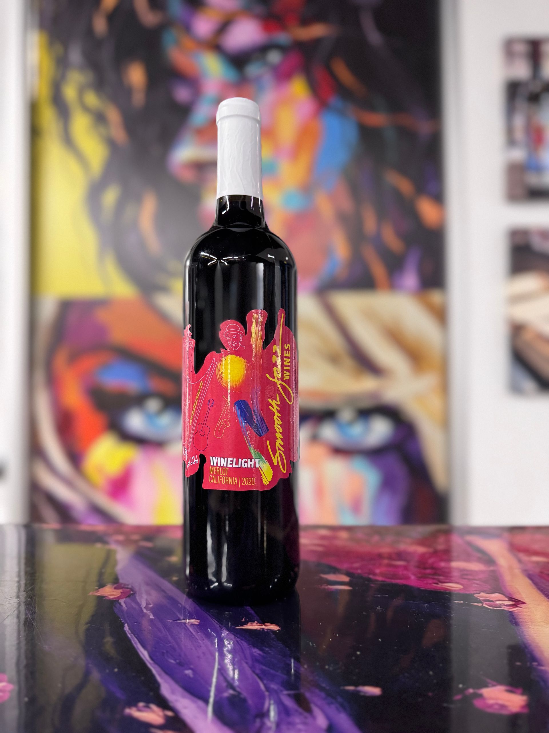 A bottle of red wine with a vibrant, abstract art label, displayed against a colorful, painted background.