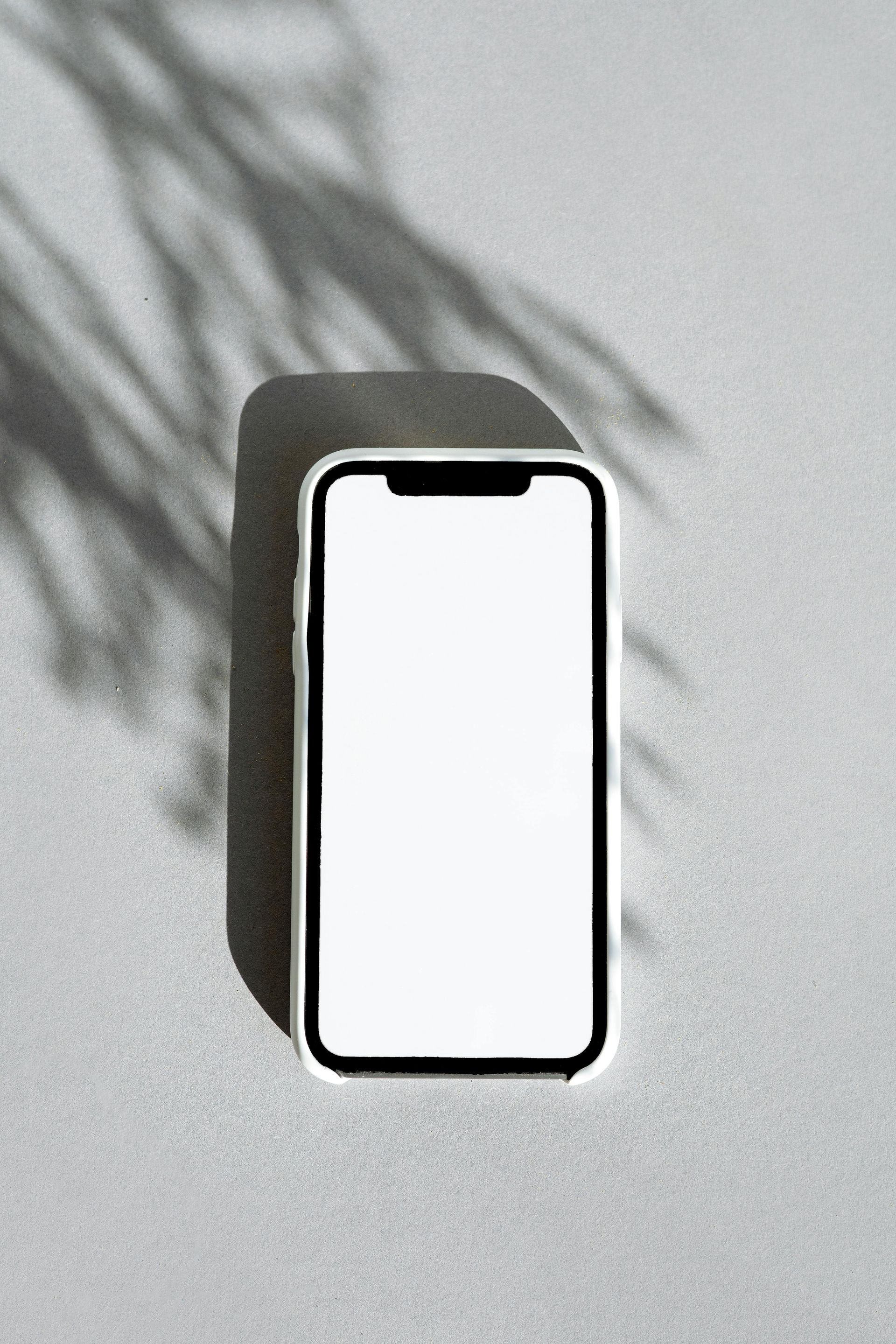 A cell phone with a white screen is sitting on a table with a shadow of a palm tree.