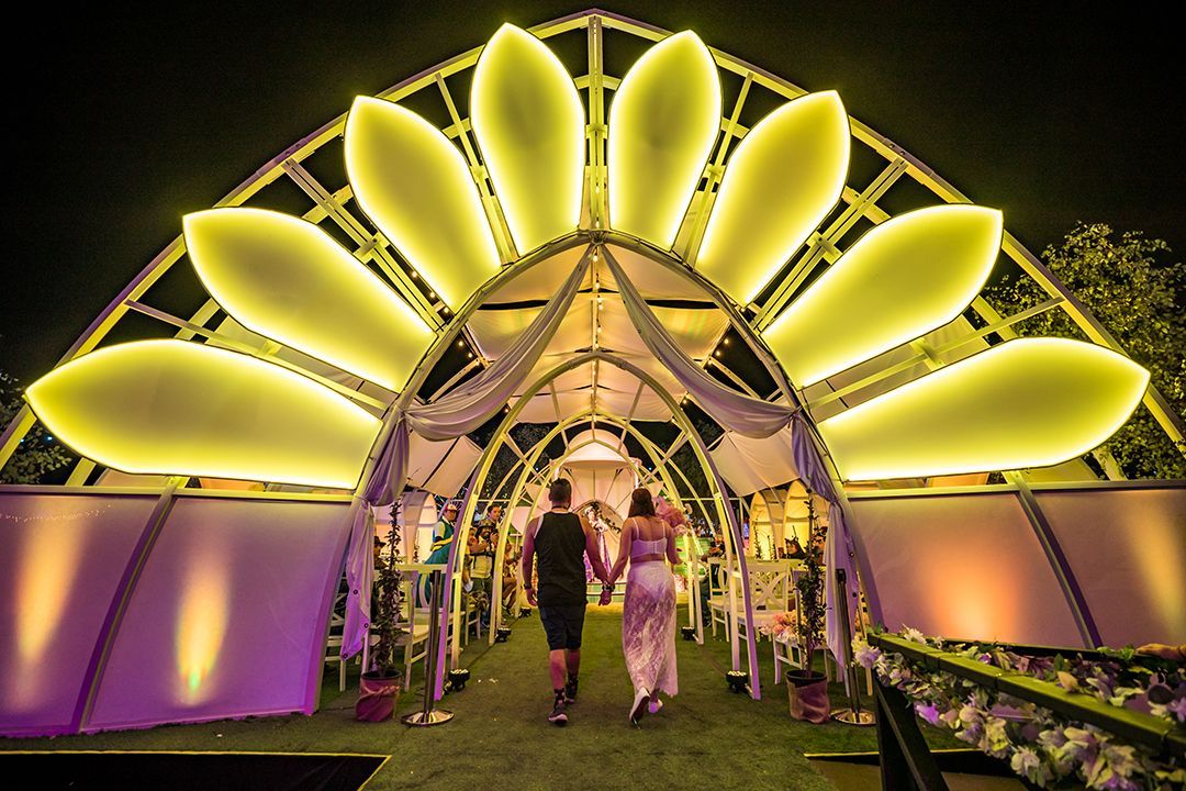 A man and a woman are walking under a large yellow and purple archway at EDC, the Electric Daisy Carnival.