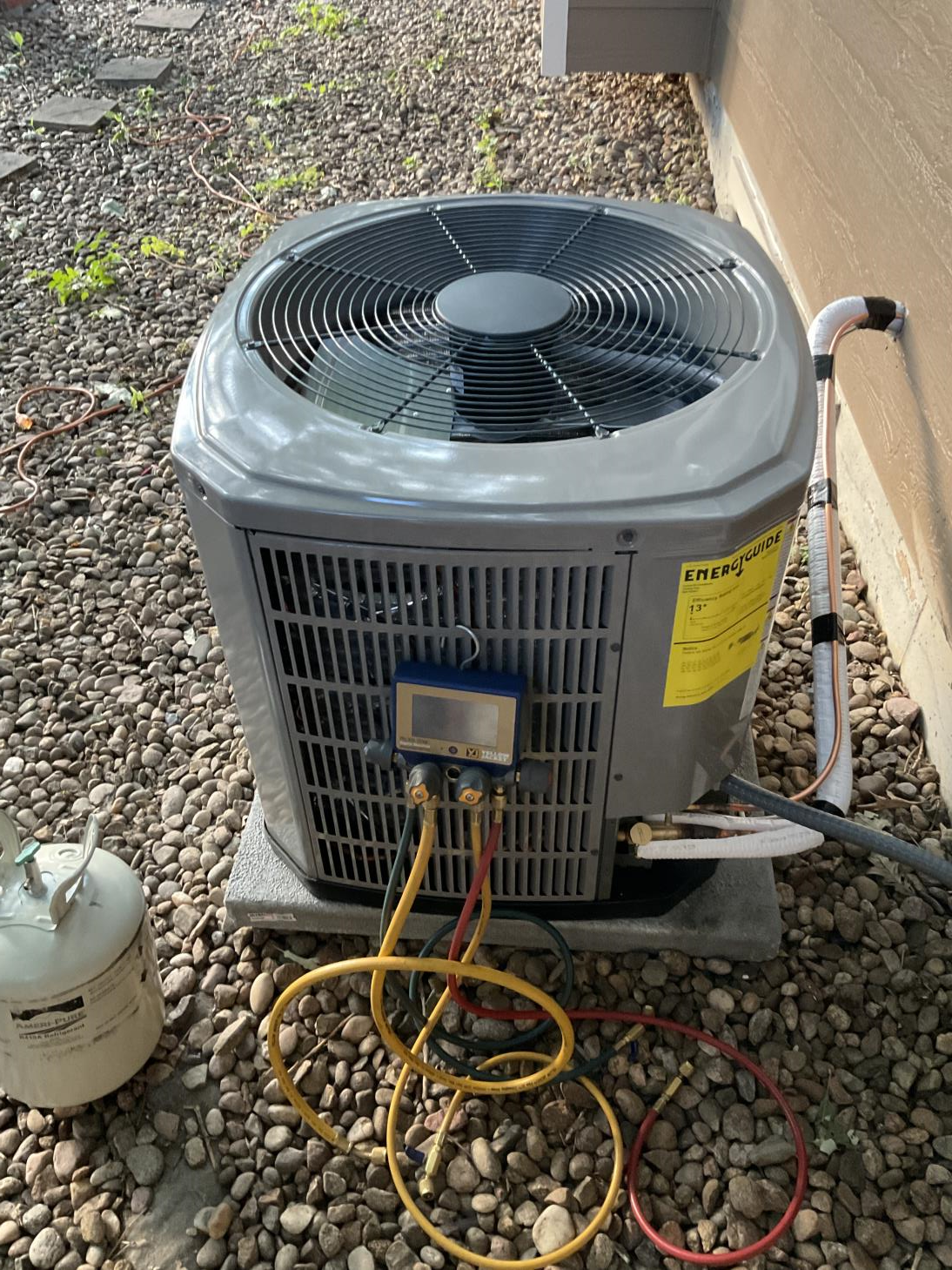 An air conditioner is sitting on top of a pile of rocks next to a propane tank.