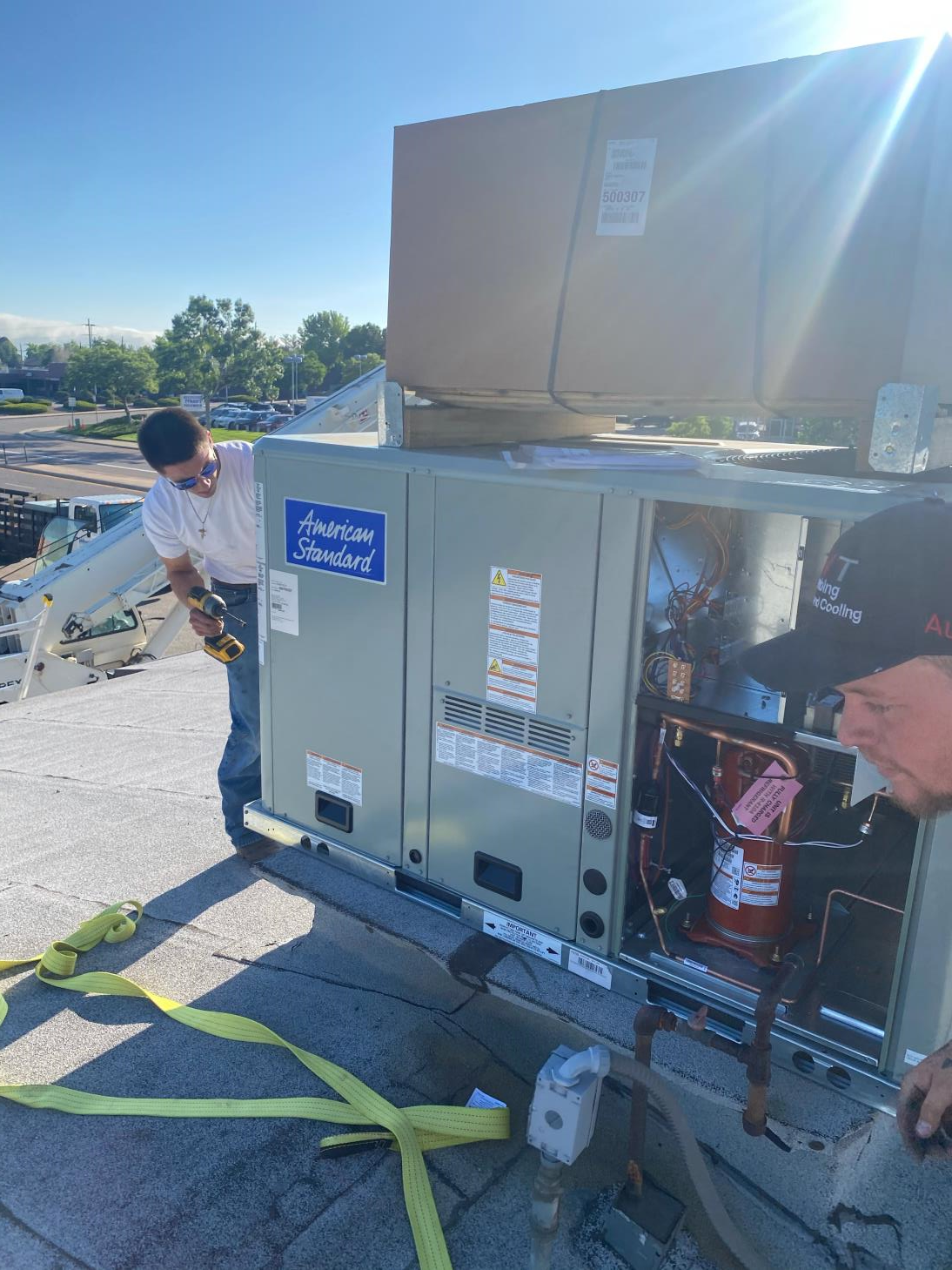Two men are working on an air conditioner on top of a roof.