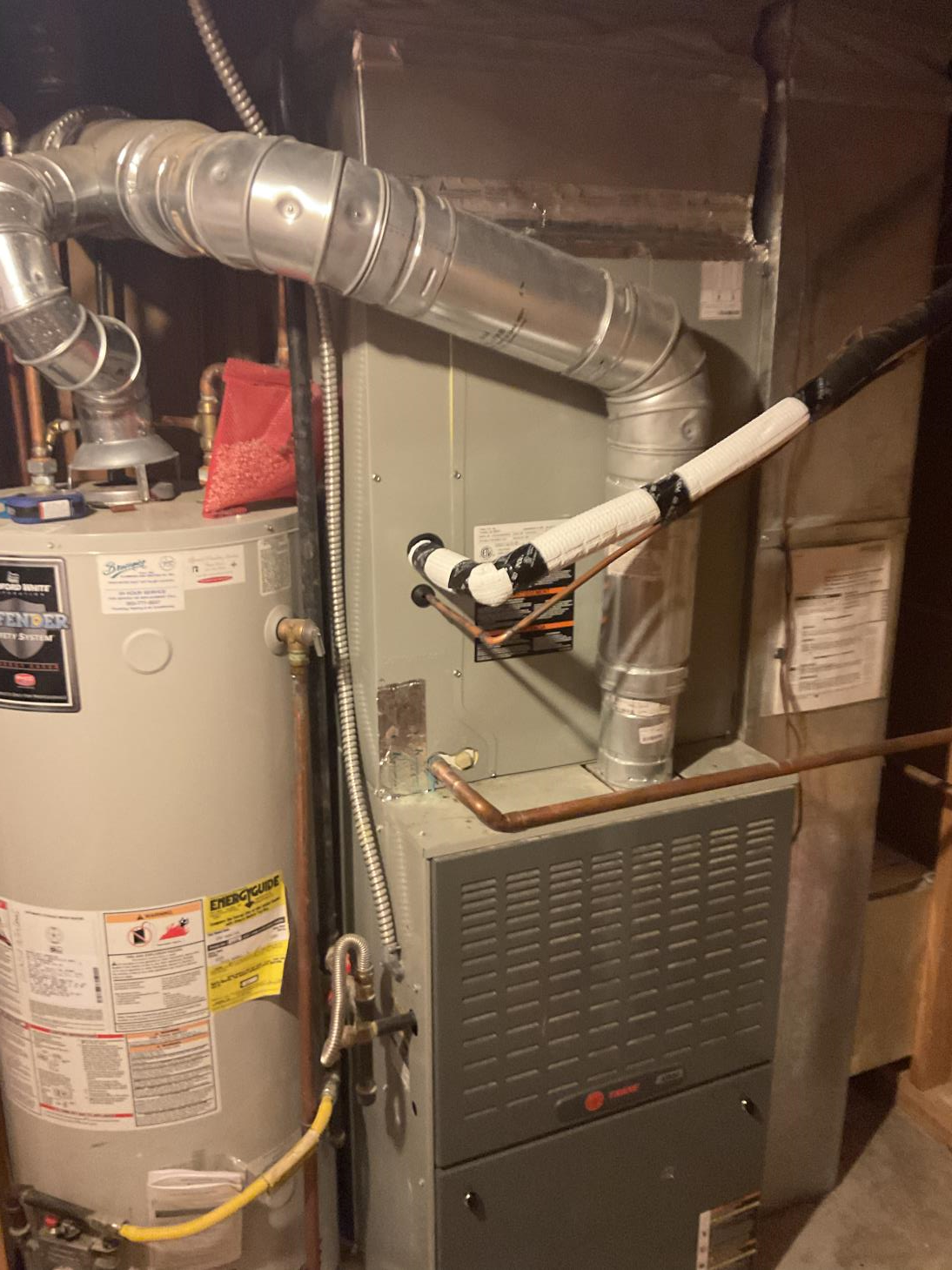 A water heater is sitting next to a furnace in a basement.