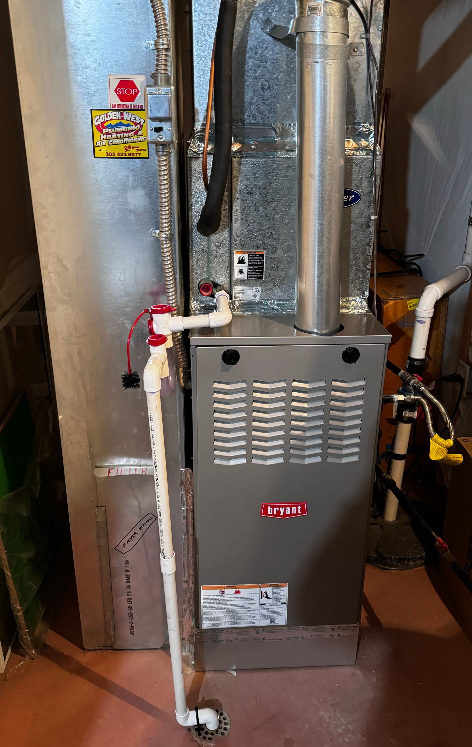 A furnace is sitting in a basement next to a pipe.