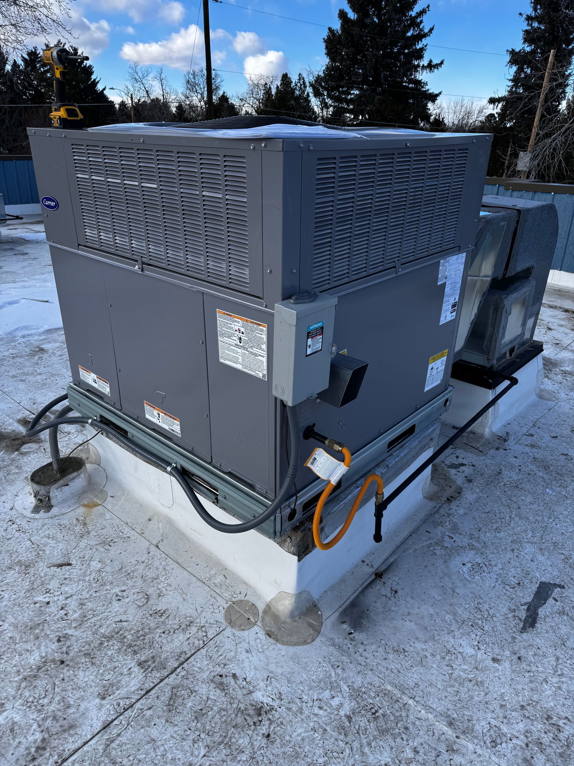 A large air conditioner is sitting on top of a snow covered roof.