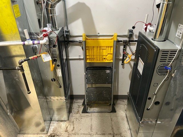 A yellow ladder is sitting in a room next to a furnace.