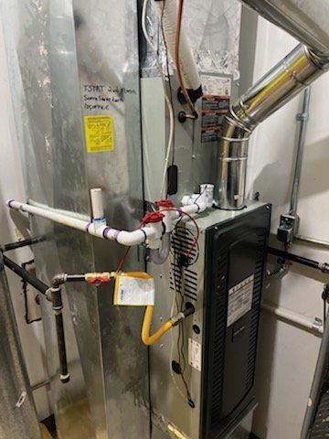 An air conditioner is sitting in a room next to a pipe.