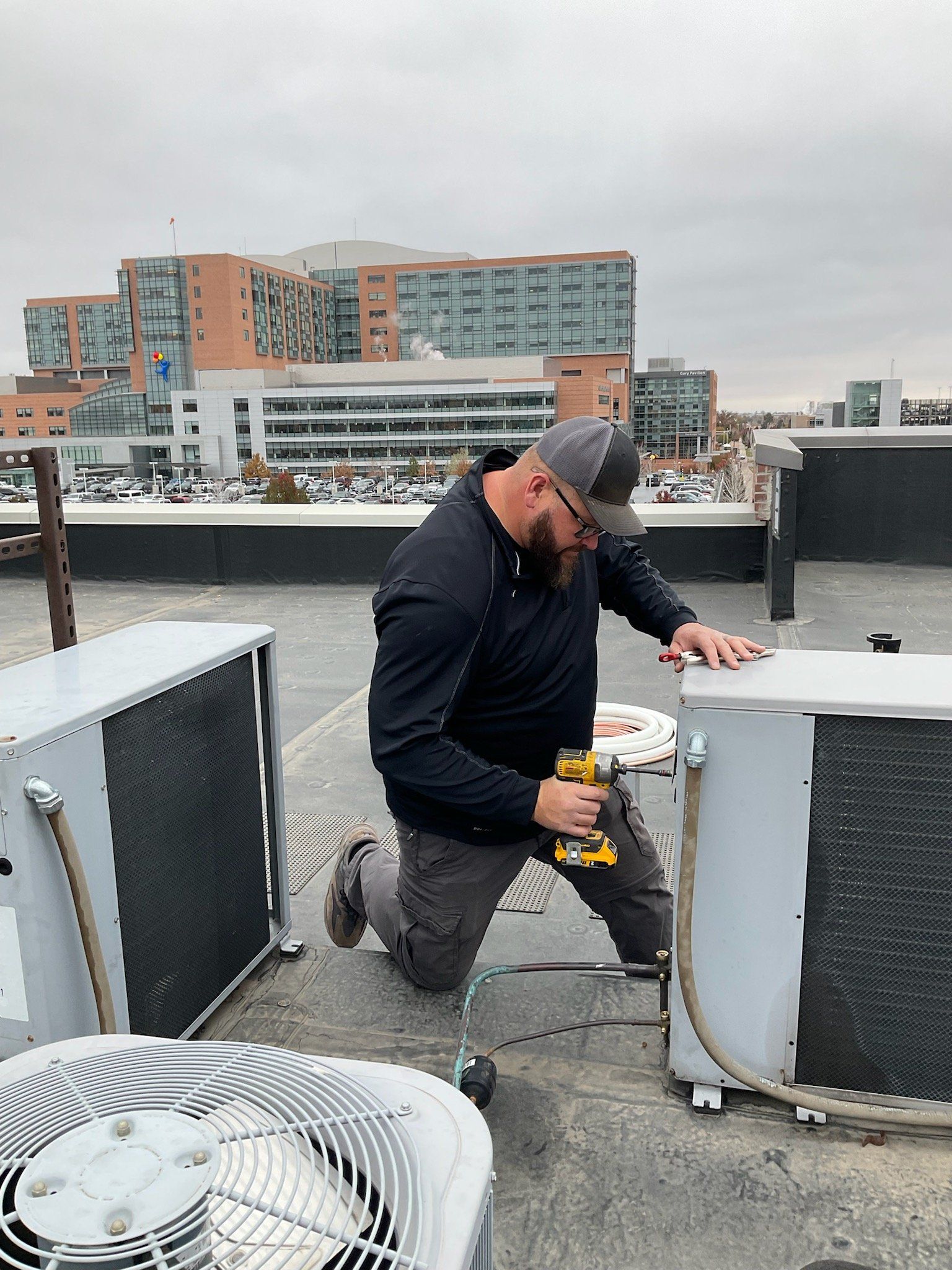 A man is working on a rooftop air conditioner with a drill.