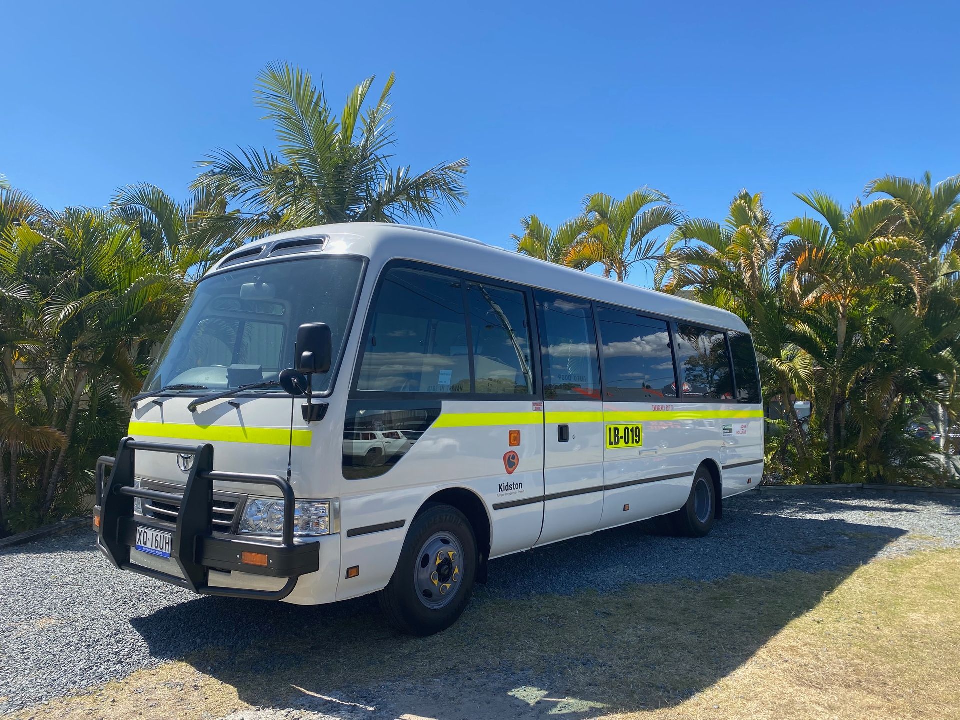 A white bus with yellow stripes on the side is parked in a gravel lot.