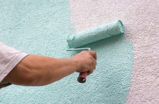 Person painting a textured white wall with a turquoise paint roller.