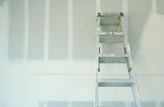 Ladder leaning against a white wall with exposed studs, indoors.