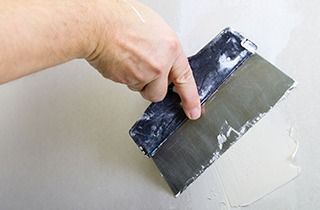 Hand using a putty knife to apply spackle to a wall.