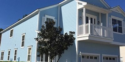 A two-story, blue house with white trim and a small balcony. A tree is in front.