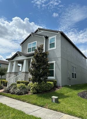 Two-story gray house with a porch, green lawn, and blue sky.