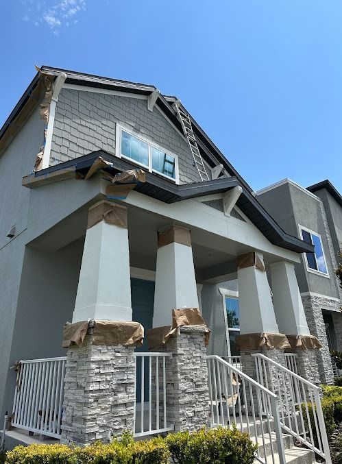 Two-story house with light blue paint, white pillars, and stone accents; blue sky.