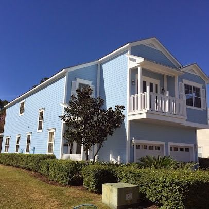 Blue two-story house with white trim, balcony, and garage doors; set against a clear blue sky.