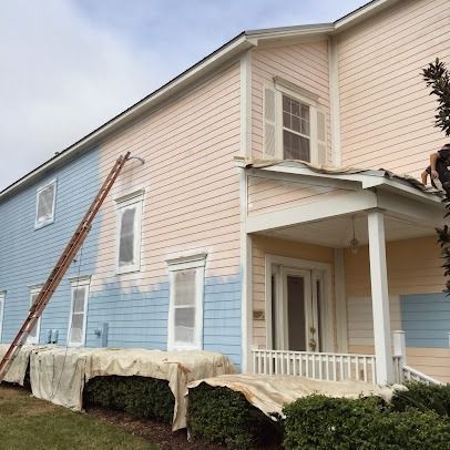 House being painted, blue on the left and pink/yellow on the right. Ladder and painter visible.