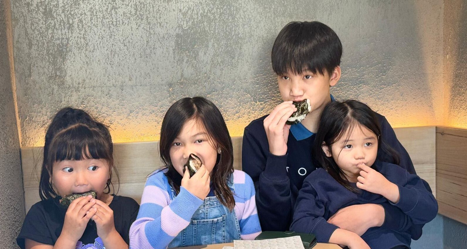 A group of children are sitting at a table eating onigiri.