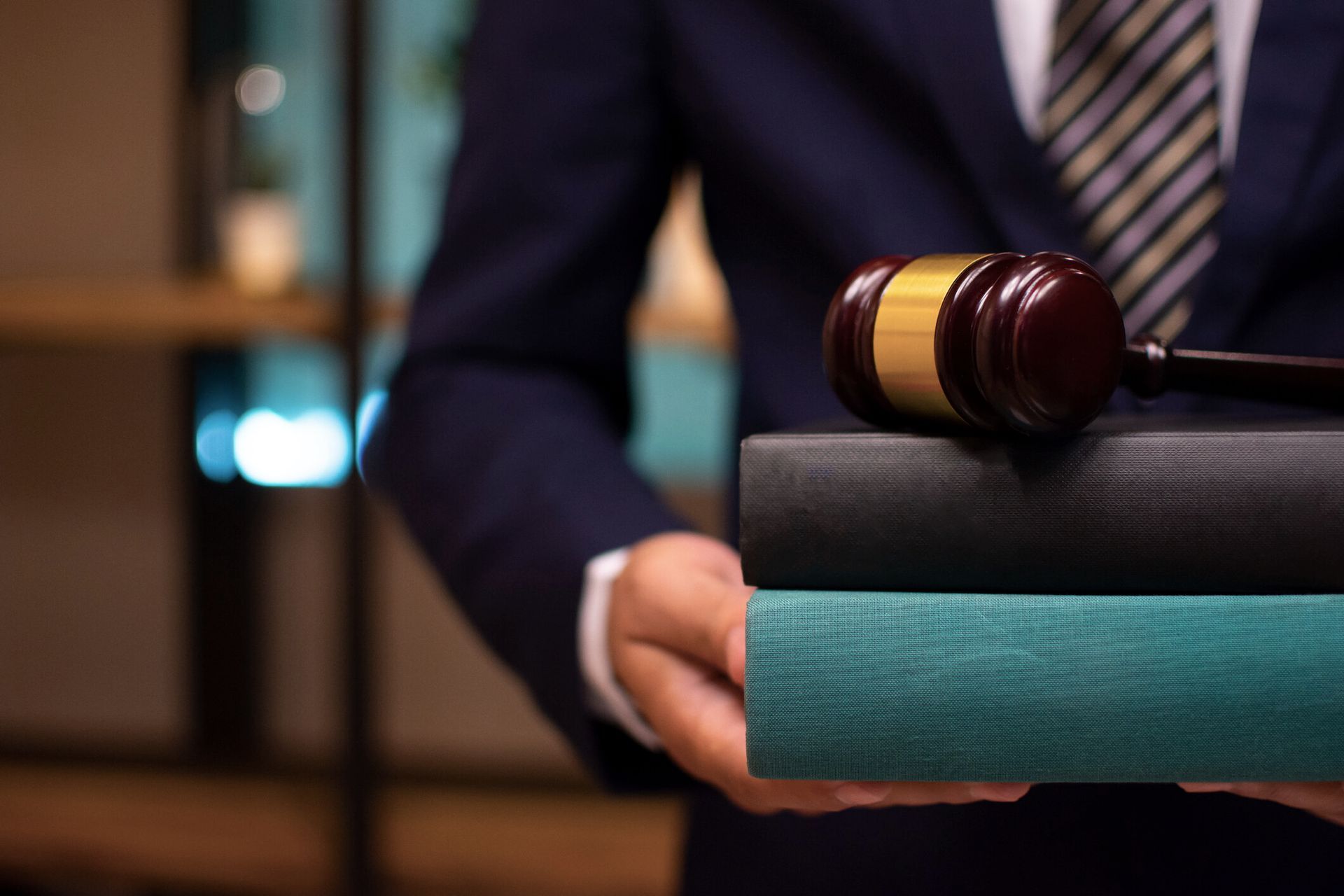 A man in a suit and tie is holding a stack of books and a judge 's gavel.
