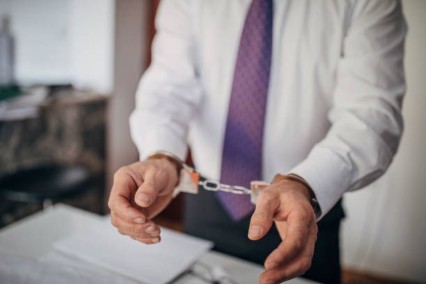 A man in a white shirt and purple tie is wearing handcuffs.
