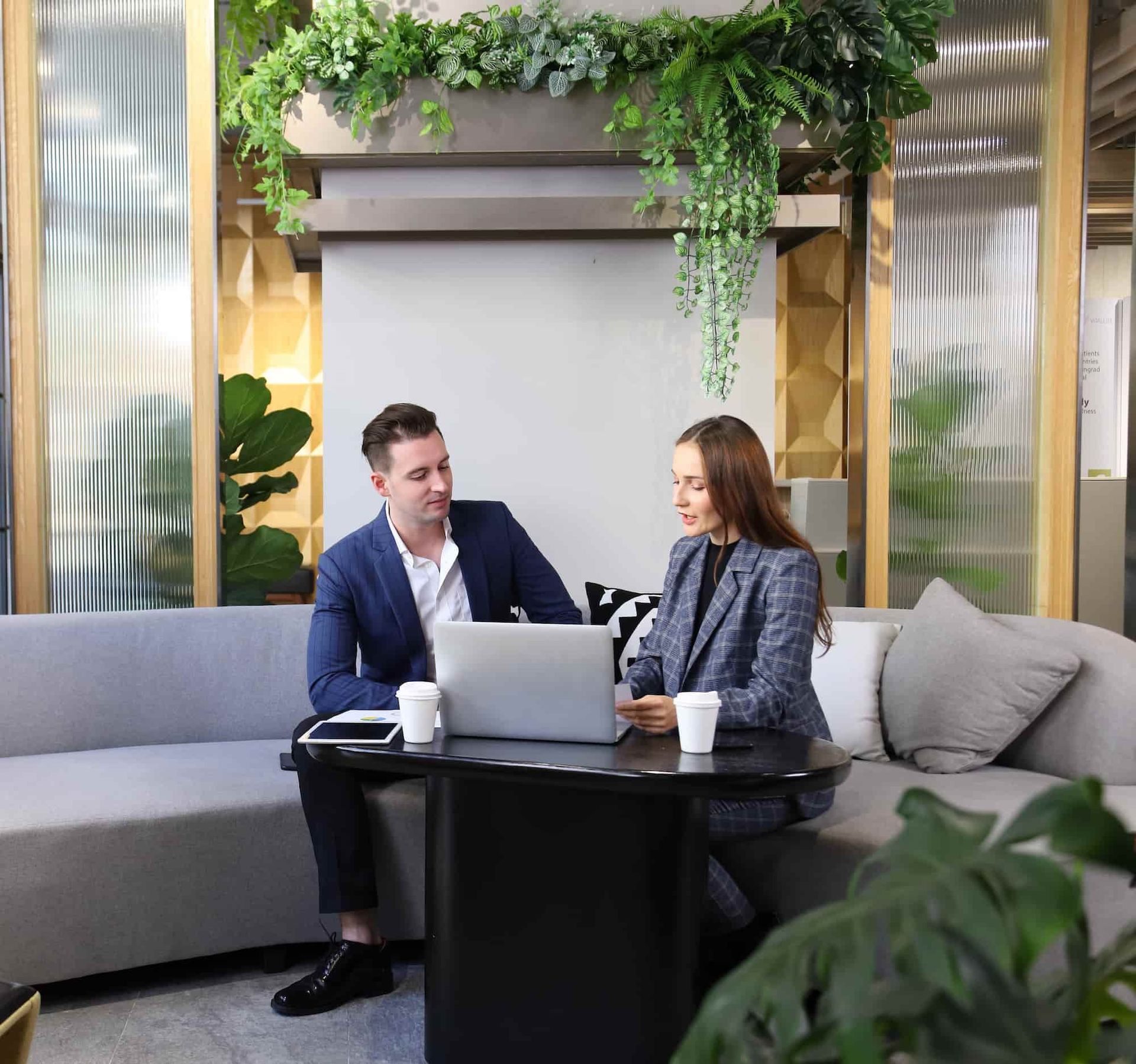Man and woman in business attire at a table with laptop, discussing.