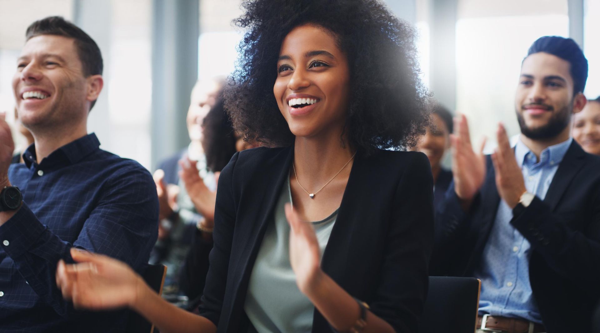 People in business attire clapping and smiling at an event.