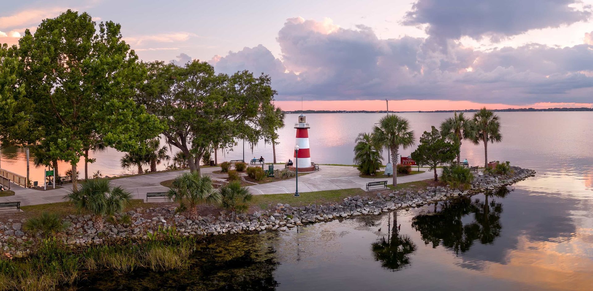 Lighthouse on a peninsula at dusk with trees and calm water; pink and purple sky.