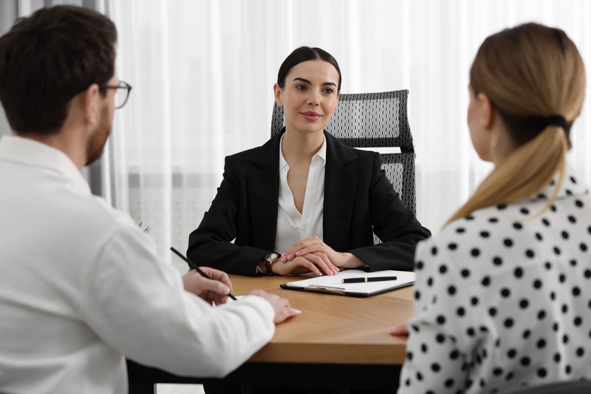 Woman in a suit at a table with a couple, possibly conducting a meeting or interview.