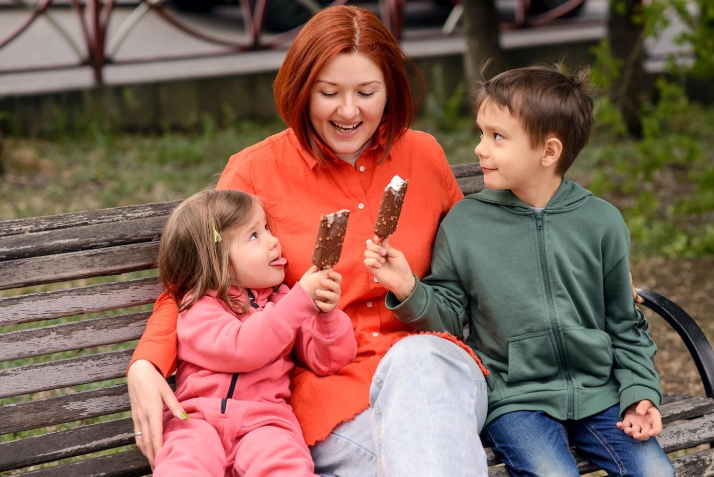 Woman and two children on bench eating ice cream.