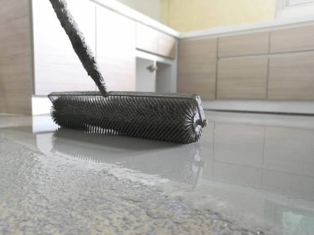 A roller is being used to paint a concrete floor in a kitchen.