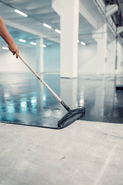 A person is painting a concrete floor with a broom.