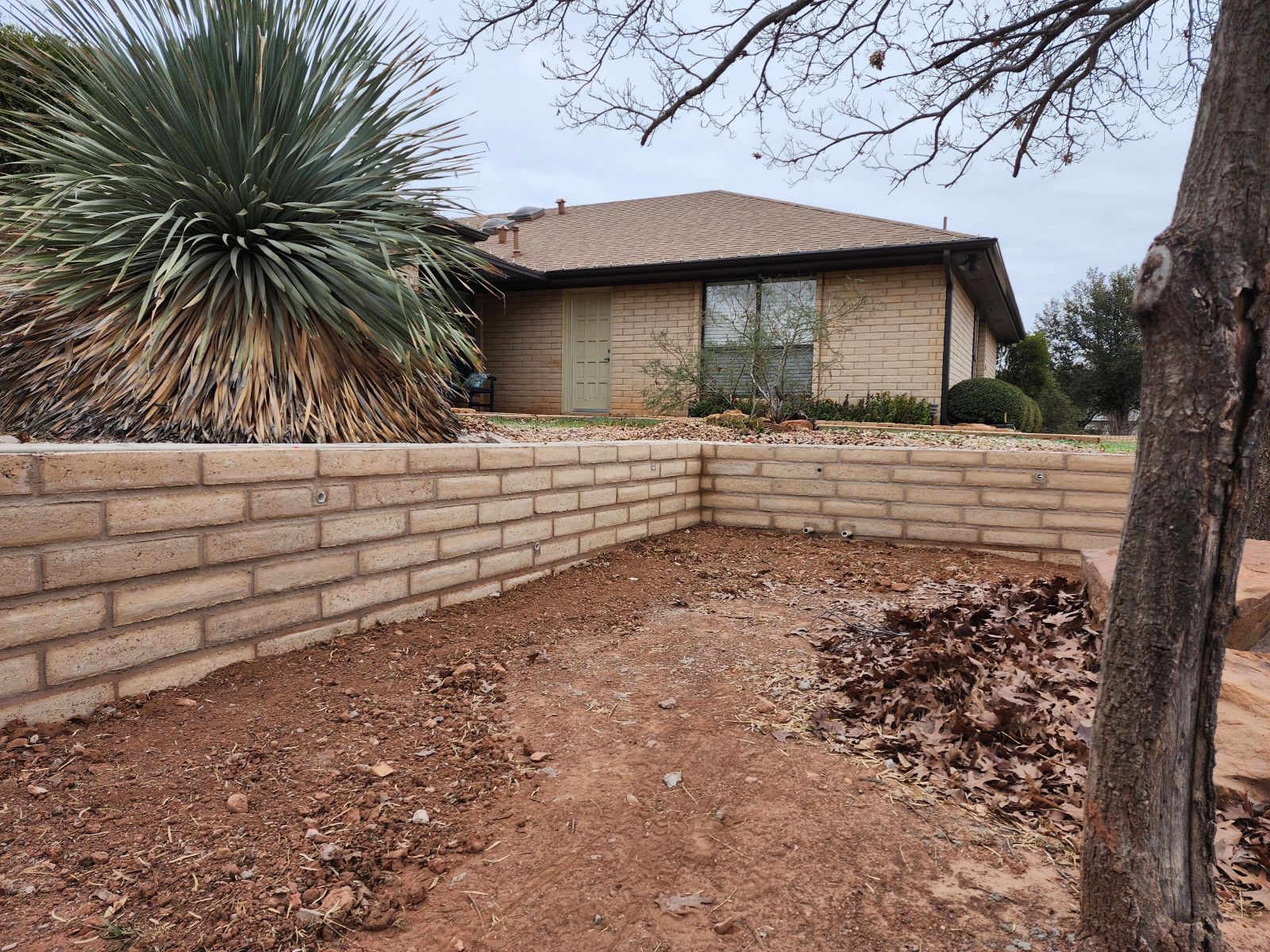 A house with a brick wall and a tree in front of it.