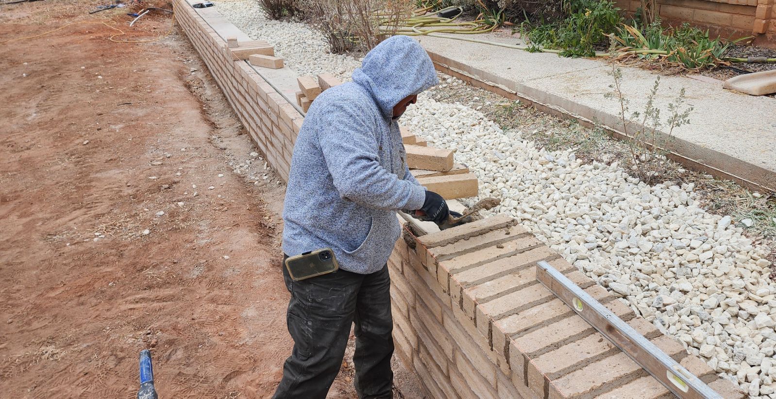 A man in a hooded jacket is working on a brick wall.