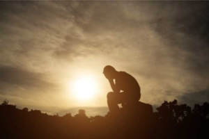 A silhouette of a man sitting on a rock at sunset.