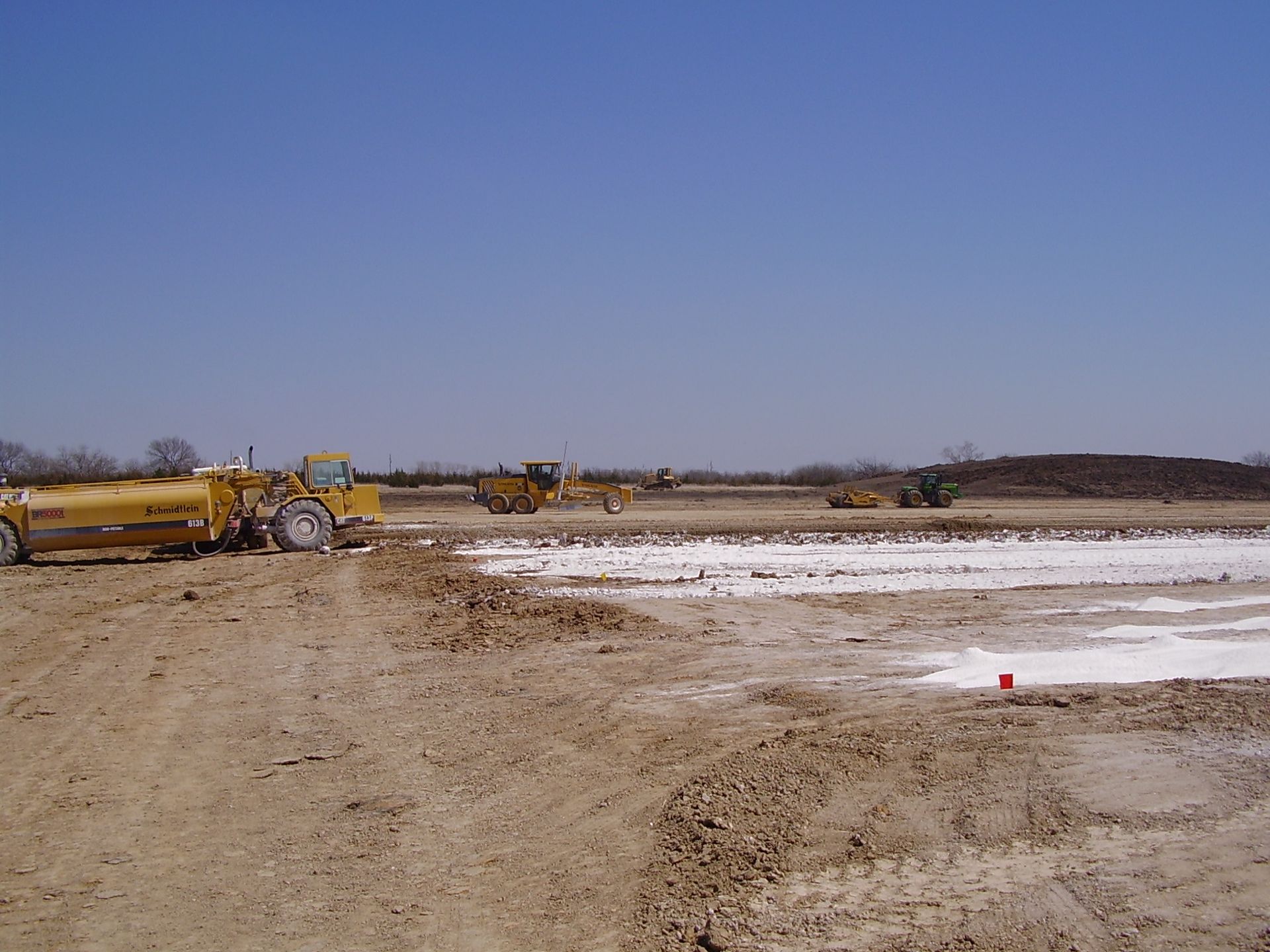 A group of construction vehicles are parked in a dirt field.