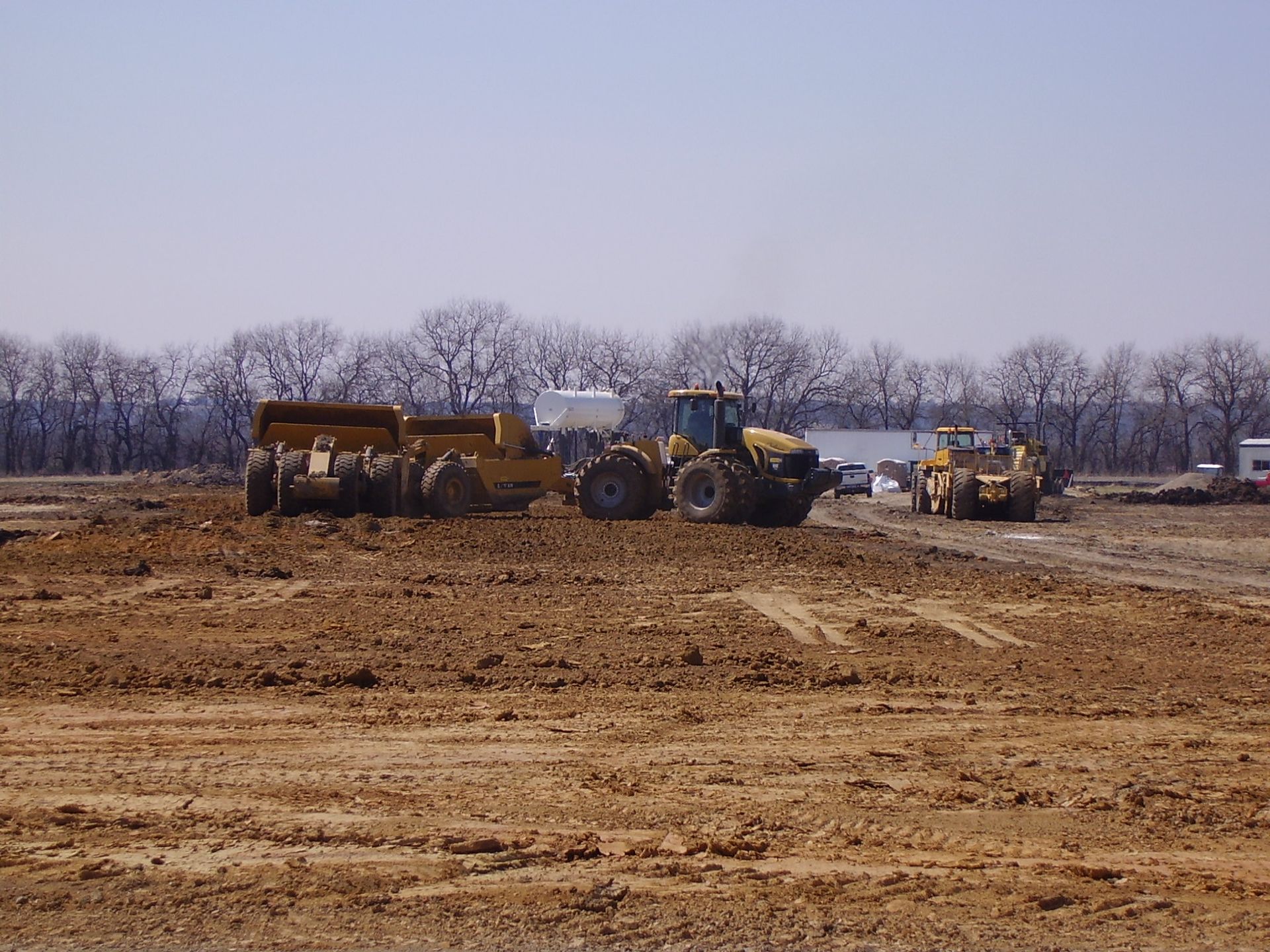 A group of construction vehicles are working in a dirt field