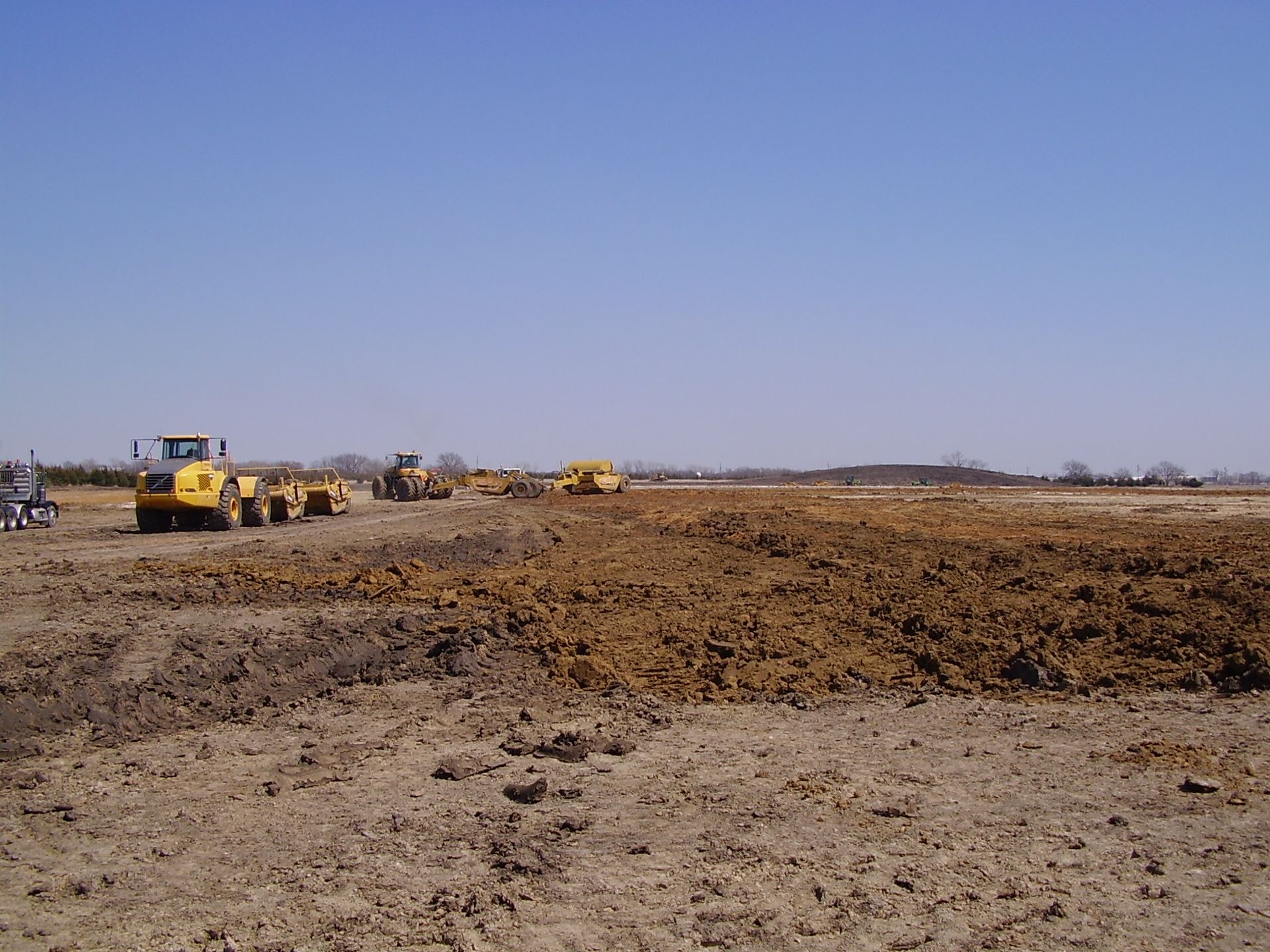 A group of construction vehicles are working on a dirt field.