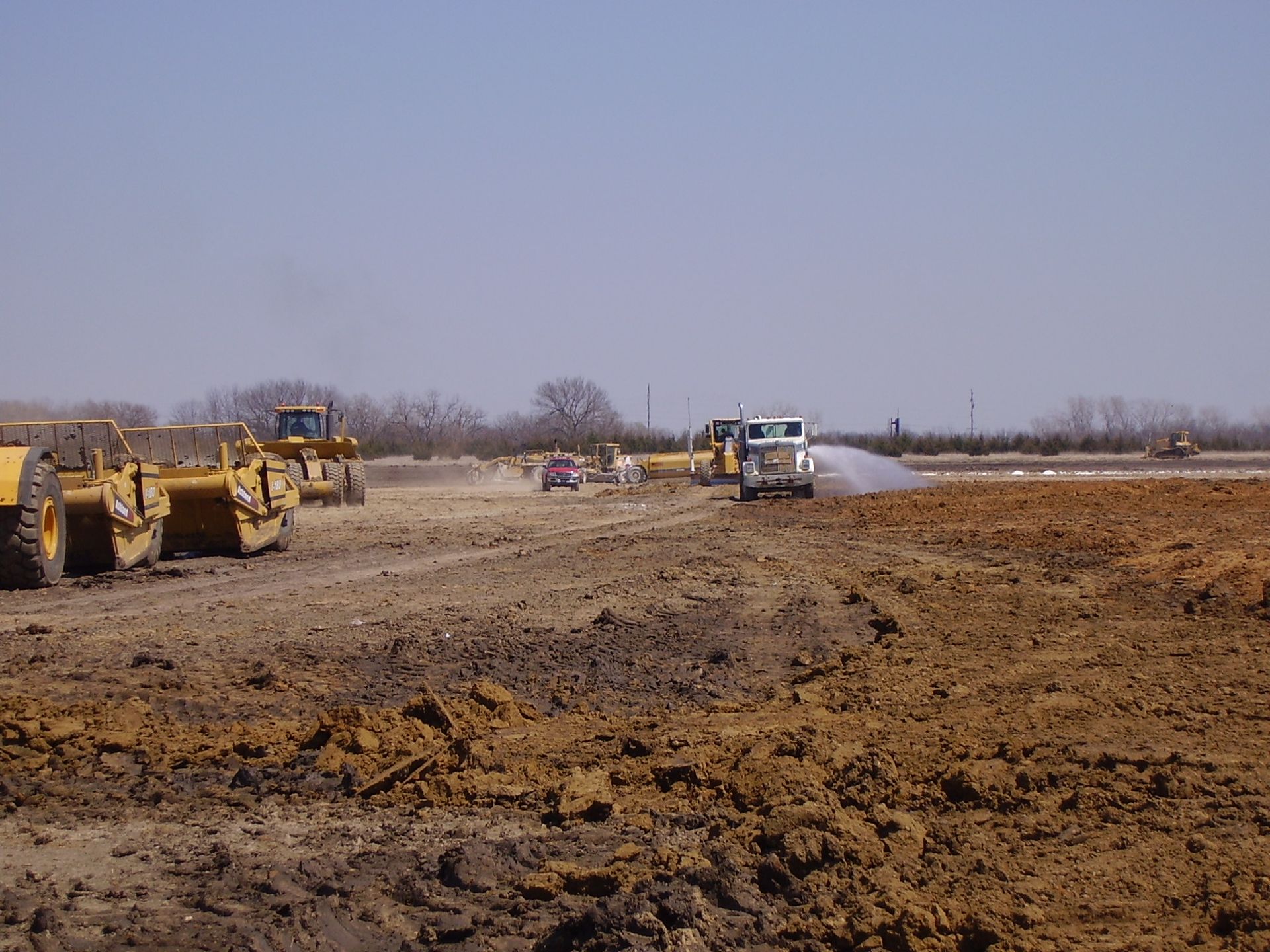 A group of construction vehicles are working on a dirt field.