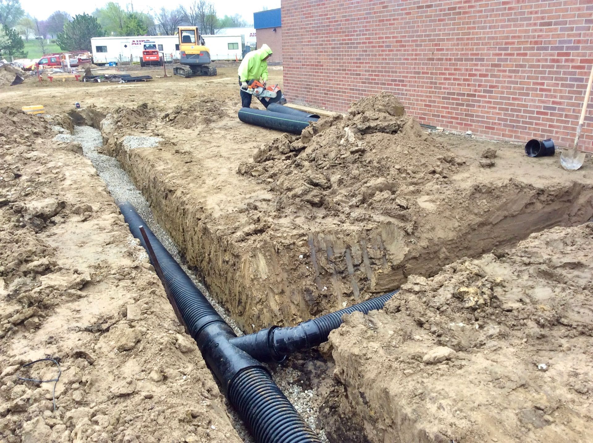 A man is laying pipes in the dirt in front of a brick building.