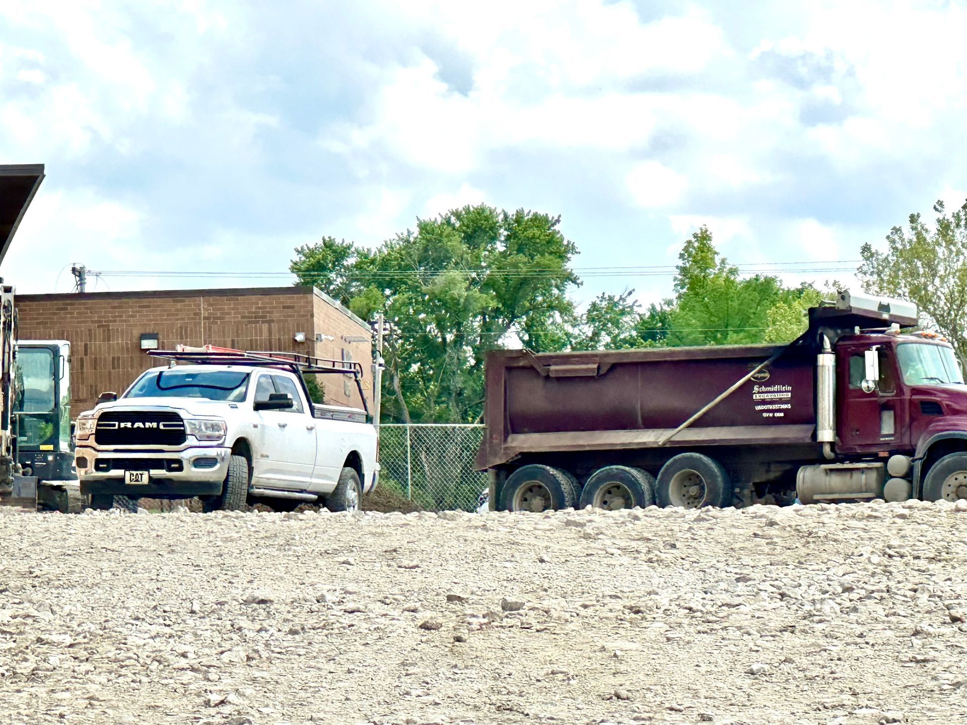 A dump truck is driving down a dirt road next to a white truck.